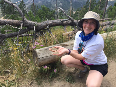 Scientist kneeling along path in mixed prairie and wooded area with sandy soil in hand