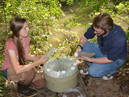 Two researchers crouch next to a carousel of 24 water samples.