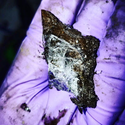 A gloved hand holds a shard of permafrost soil with ice crystals jutting up