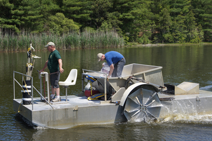 Resarchers in barge applying aluminum sulfate to a holding pond in summer